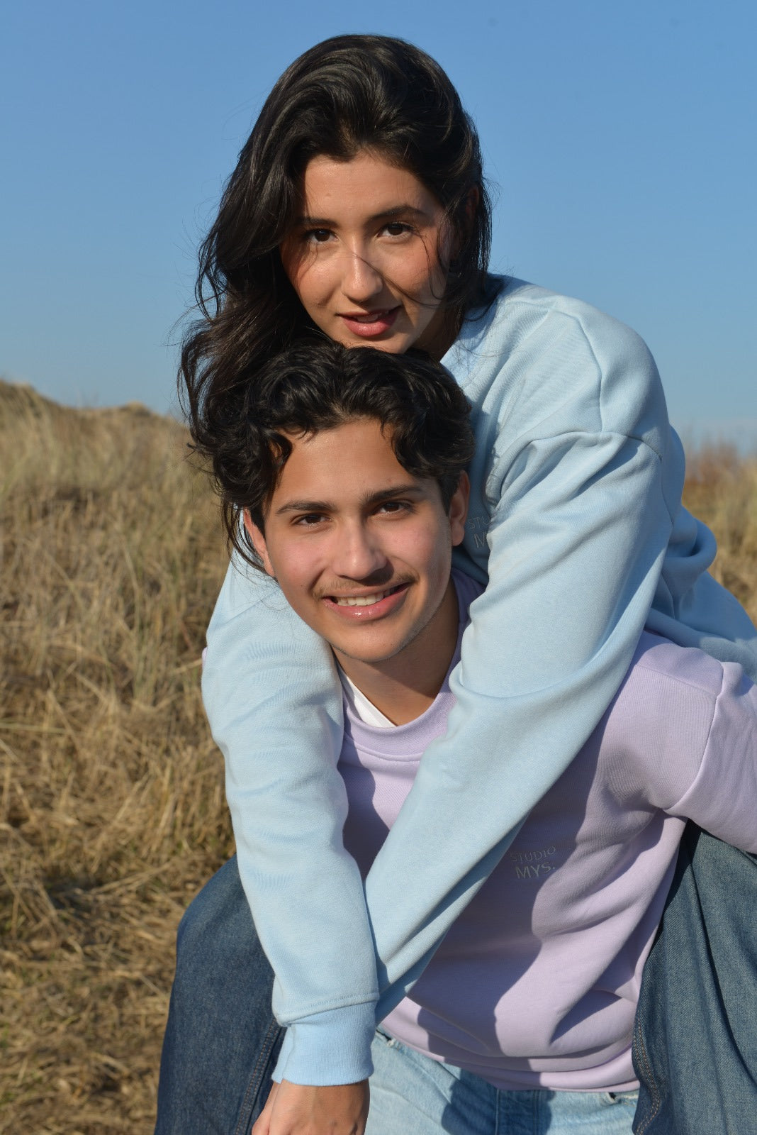 Couple enjoying a sunny day outdoors, showcasing stylish relaxed fit sweaters in lila and light blue.